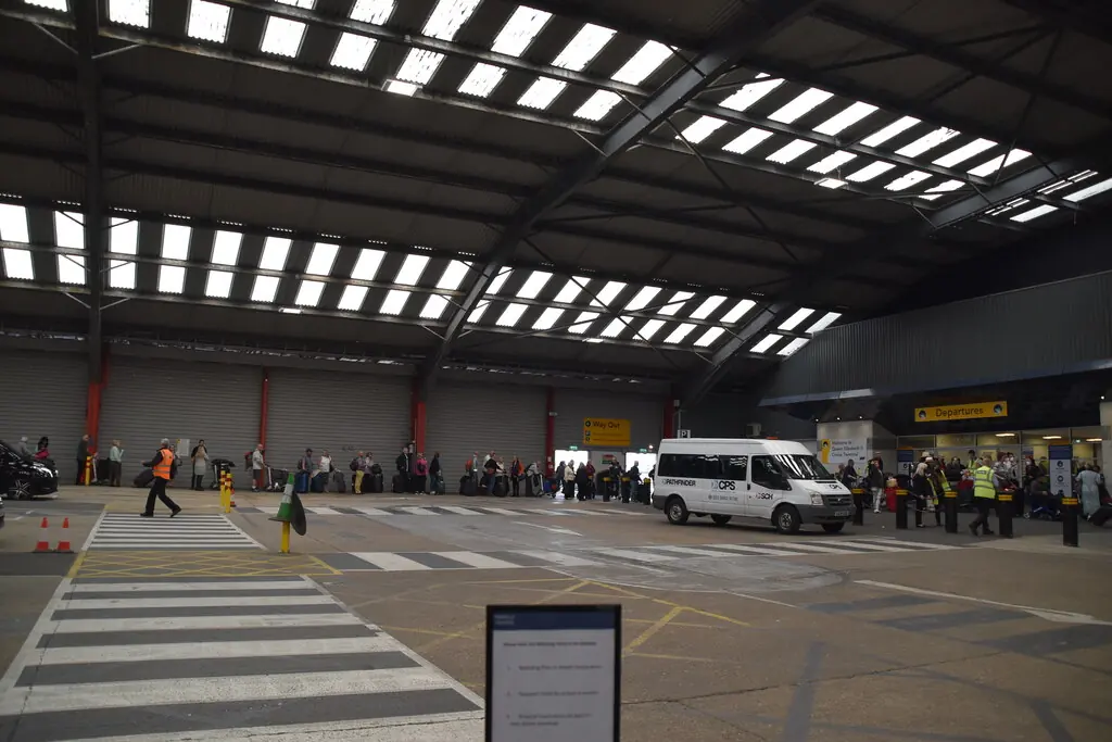 Passengers with luggage queuing in the covered drop-off hall inside the QEII Cruise Terminal