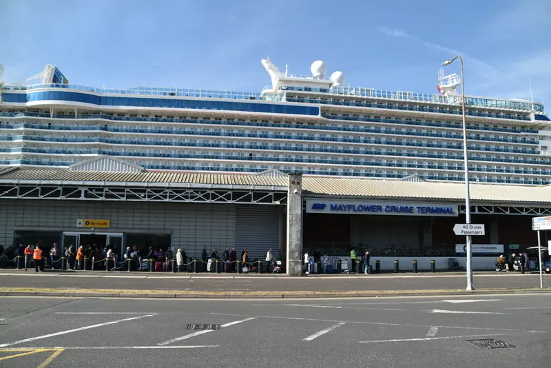 Passengers queuing outside the Mayflower Cruise Terminal with a cruise ship berthed behind
